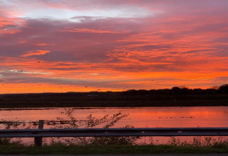 Impresionante atardecer sobre el lago en glamping, el cielo resplandece en tonos vivos de naranja y rosado.