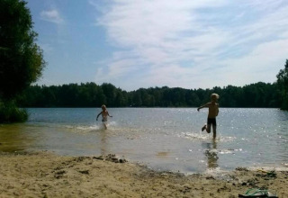 Due bambini giocano sulla riva di un lago sotto il sole in una struttura glamping immersa nella natura.