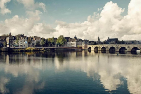 View of a river, historic buildings, and a stone bridge taken from a glamping accommodation by the water.