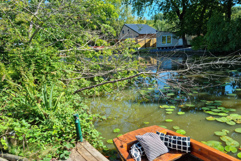 Vista de un estanque con lirios de agua, árboles y el chalet Casita La Luna en Bélgica.
