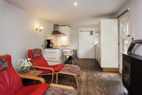 Gezellige woonkamer van ‘The Wijerschans’ in België met rode stoelen, keukenhoek en houtkachel.