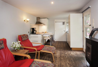 Gezellige woonkamer van ‘The Wijerschans’ in België met rode stoelen, keukenhoek en houtkachel.