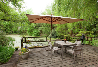 Houten terras met tafel, stoelen en parasol uitkijkend op een vijver bij «The Wijerschans» in België.