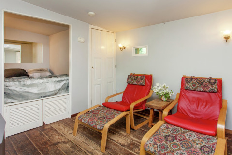 Knusse Vlaamse cabin in België, met twee rode stoelen, tafeltje met bloemen en hoekbed in een nis.