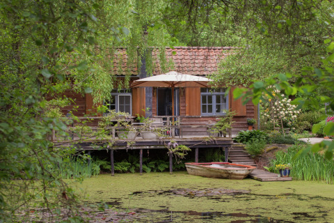 Gezellige hut aan een vijver in België, met terras, bootje en weelderig omgeven door groen.