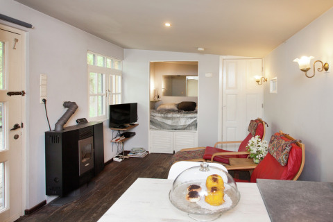 Knusse woonkamer in cabin The Wijerschans in België, met haard, tv, zitjes en zicht op slaapkamer.