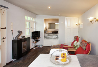 Knusse woonkamer in cabin The Wijerschans in België, met haard, tv, zitjes en zicht op slaapkamer.