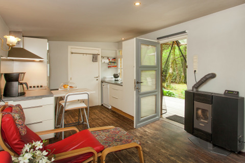 Knus interieur van The Wijerschans-hut in België met keuken, houtkachel en zicht op de groene tuin.