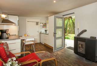 Knus interieur van The Wijerschans-hut in België met keuken, houtkachel en zicht op de groene tuin.