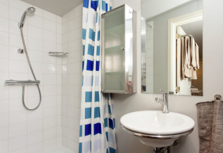 Moderne badkamer in de hut The Wijerschans in België, met douche, wasbak, spiegel en blauw geruit gordijn.