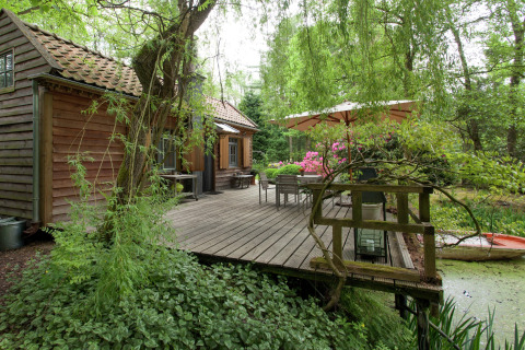 Houten cabin met terras en parasol aan een vijver, omgeven door groen, The Wijerschans, België.