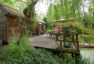 Houten cabin met terras en parasol aan een vijver, omgeven door groen, The Wijerschans, België.