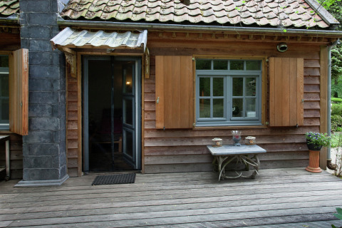 The Wijerschans hut in België, met houten gevel, open luiken en een houten terras midden in het groen.