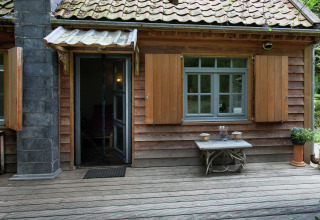 The Wijerschans hut in België, met houten gevel, open luiken en een houten terras midden in het groen.