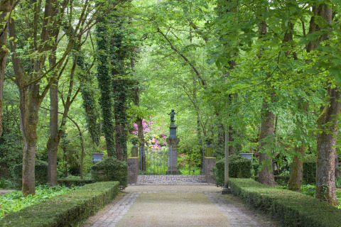 Pad door een weelderige tuin met beeld en smeedijzeren hek bij The Wijerschans, België.