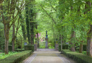 Pad door een weelderige tuin met beeld en smeedijzeren hek bij The Wijerschans, België.