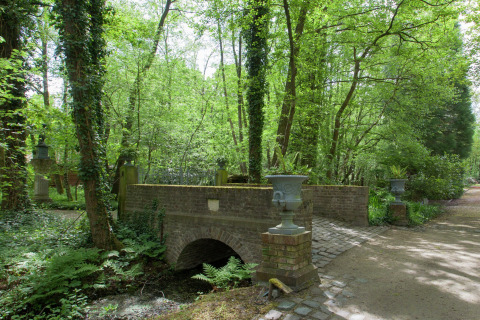 Afbeelding van een stenen brug bij het boshuis 'The Wijerschans' te midden van groen in België.