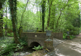 Afbeelding van een stenen brug bij het boshuis 'The Wijerschans' te midden van groen in België.