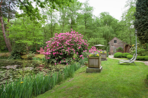 Groene tuin met vijver, bloeiende struiken en houten tuinhuis bij 'The Wijerschans' in België.