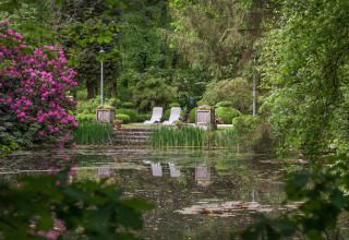 Rustige natuurlijk tuin met vijver en twee stoelen aan The Wijerschans, België, omringd door groen.