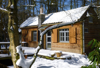 Houten huisje The Wijerschans in België, gelegen in een besneeuwd bos met zonlicht op het dak.