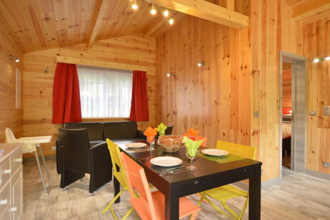 Dining area of Le Chalet Chaleureux A in Belgium with wooden walls, colorful chairs, and a cozy ambiance.