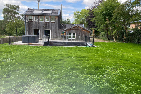 Houten lodge Le coeur du brâme met groot gazon, omheind terras en bomen op de achtergrond.