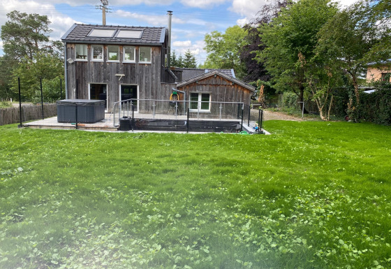 Houten lodge Le coeur du brâme met groot gazon, omheind terras en bomen op de achtergrond.