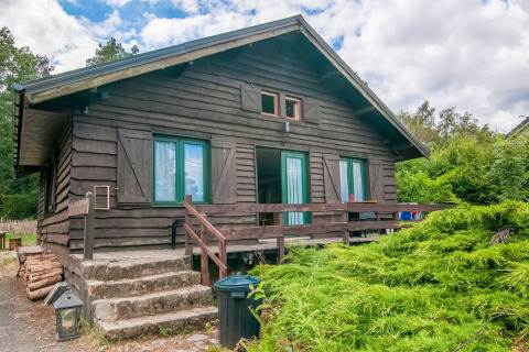 Lodge named Au Coeur du Pêcheur with wooden exterior, front steps, railing, and lush green shrubs.