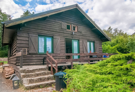 Lodge named Au Coeur du Pêcheur with wooden exterior, front steps, railing, and lush green shrubs.