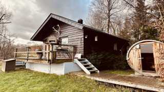 La Cabane chalet with a wooden deck and round sauna, nestled in nature and surrounded by trees and greenery.