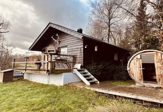 Chalet La Cabane met houten terras en ronde sauna, omgeven door bomen en groene natuur in de buitenlucht.