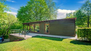 Moderne lodge Manonfa met groot terras, omgeven door groene bomen en een heldere blauwe hemel op een zonnige dag.