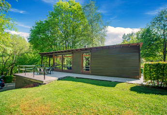 Lodge Manonfa moderno con grande terrazza, immerso nel verde degli alberi e sotto un cielo azzurro luminoso.