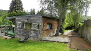 Photo of a cozy wooden chalet named Le Chaly, surrounded by lush trees and a well-kept grassy yard.