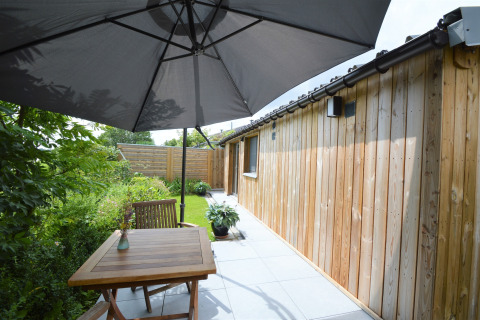 Terrasse extérieure avec table en bois, chaises et grand parasol près d’un chalet au Chalet de Bioul, Belgique.