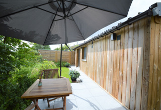 Terrasse extérieure avec table en bois, chaises et grand parasol près d’un chalet au Chalet de Bioul, Belgique.