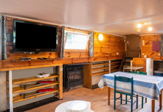 Woonruimte op woonboot 'Le Bateau du Lac Privé' in België met houtafwerking, eettafel en televisie.