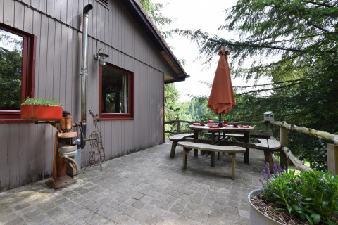 Udendørs terrasse ved Chalet Flons et Roulotte i Belgien med havebord, træbænk og udsigt til skov.