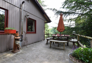 Udendørs terrasse ved Chalet Flons et Roulotte i Belgien med havebord, træbænk og udsigt til skov.