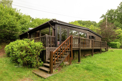 Foto van Le Chession-lodge met houten veranda, trap en veel groen in een rustige, natuurlijke omgeving.
