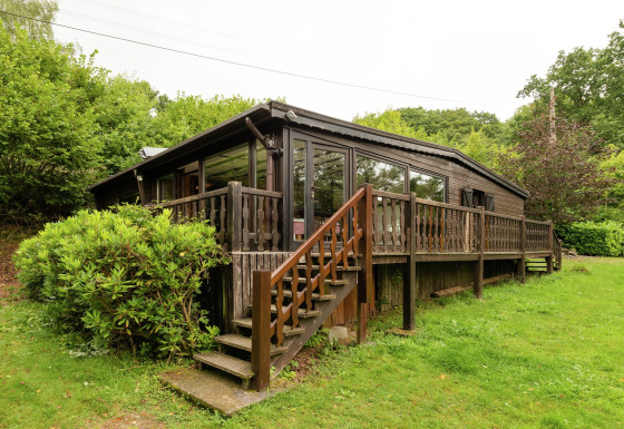 Foto van Le Chession-lodge met houten veranda, trap en veel groen in een rustige, natuurlijke omgeving.