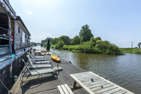 Liegestühle und Kajak auf dem Holzdeck des Hausboots 'St Antoine' an einem Fluss in Belgien.