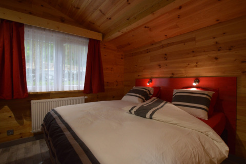 Cozy bedroom with wooden walls, red headboard, and striped bedding at Le Chalet Chaleureux A, Belgium.