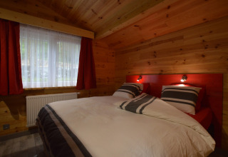 Cozy bedroom with wooden walls, red headboard, and striped bedding at Le Chalet Chaleureux A, Belgium.