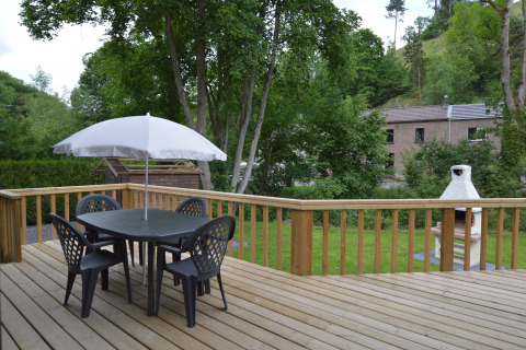 Outdoor terrace at Le Chalet Chaleureux A in Belgium with table, chairs, white umbrella, and garden view.