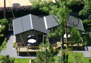 Two modern glamping cabins with deck seating and umbrellas, nestled among lush trees and landscaped lawn.