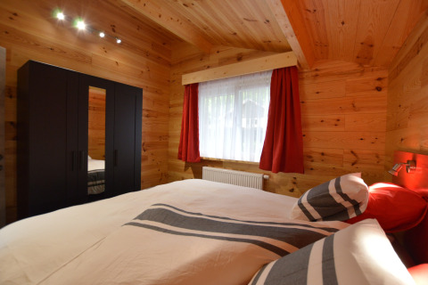 Bedroom at Le Chalet Chaleureux A in Belgium with wooden walls, black wardrobe, and striped bedding set.