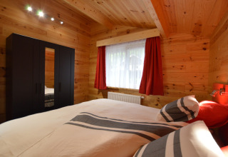 Bedroom at Le Chalet Chaleureux A in Belgium with wooden walls, black wardrobe, and striped bedding set.