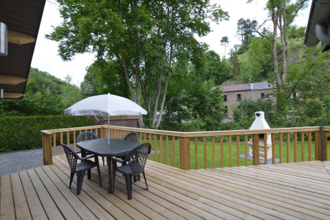 Wooden deck at Le Chalet Chaleureux A in Belgium with outdoor dining set, umbrella, and garden view.